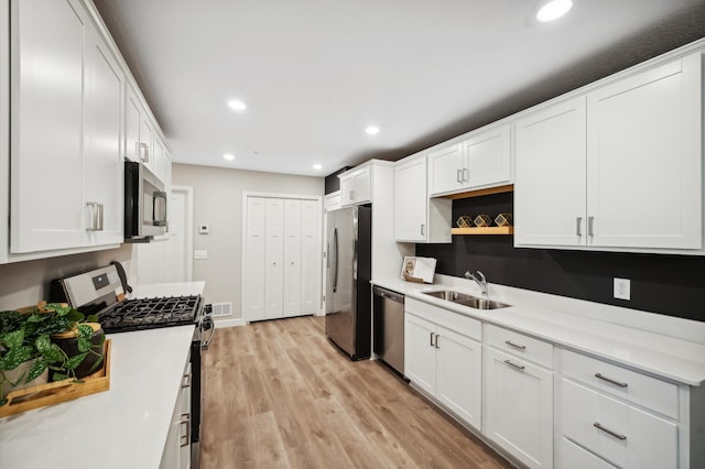 kitchen with stainless steel appliances, white cabinetry, sink, and light wood-type flooring