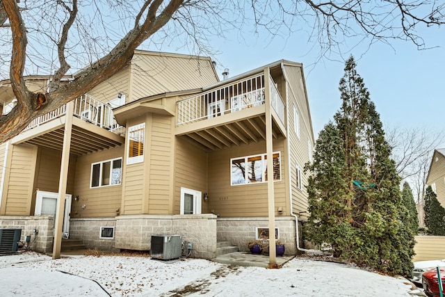 snow covered rear of property with central AC and a balcony