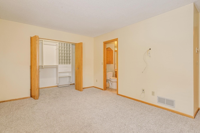 unfurnished bedroom with a closet, ensuite bathroom, light carpet, and a textured ceiling