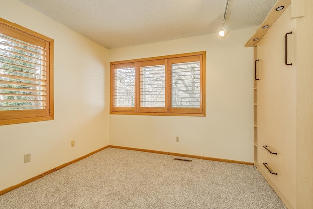 carpeted empty room featuring rail lighting and a textured ceiling