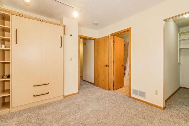 unfurnished bedroom with rail lighting, a walk in closet, light carpet, a textured ceiling, and a closet