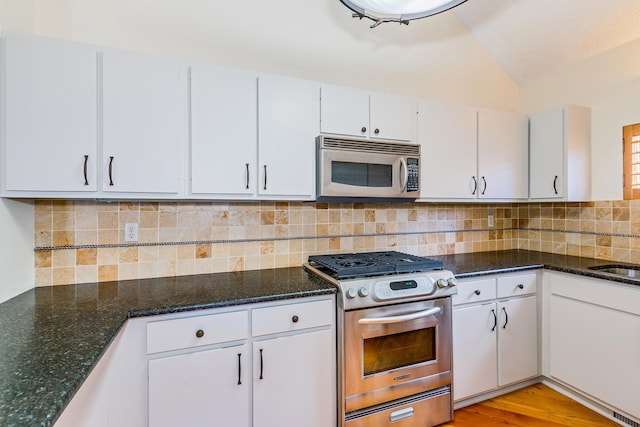 kitchen featuring appliances with stainless steel finishes, lofted ceiling, dark stone countertops, white cabinets, and decorative backsplash