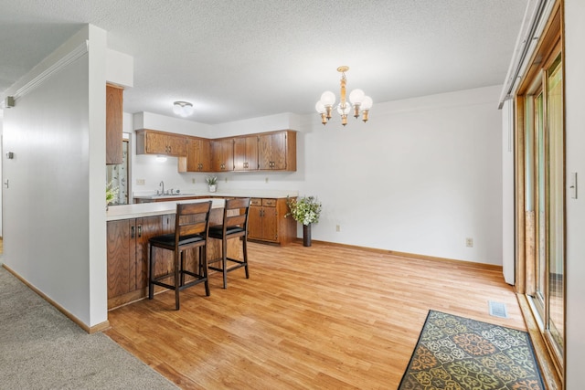 1541 2nd Ave SE, Cambridge, MN 55008 - kitchen with light countertops, brown cabinetry, a chandelier, a peninsula, and a breakfast bar area