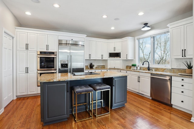 kitchen with sink, white cabinetry, built in appliances, a kitchen island, and light stone countertops