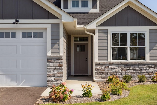 property entrance with board and batten siding, stone siding, roof with shingles, and a garage