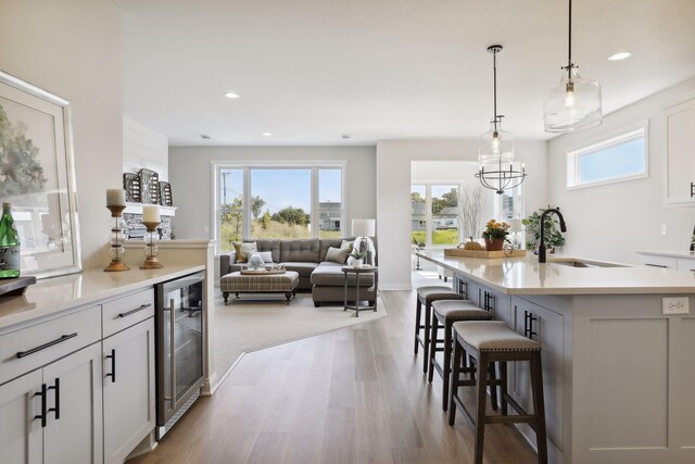 kitchen with wine cooler, a center island with sink, light countertops, a sink, and a kitchen bar