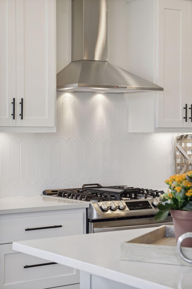 kitchen with gas stove, light countertops, wall chimney range hood, and white cabinetry