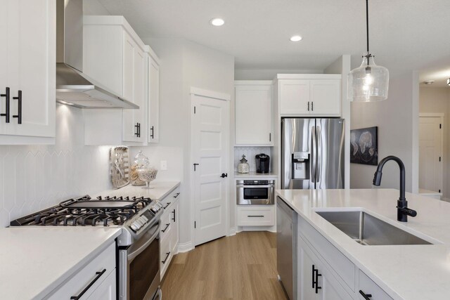 kitchen featuring stainless steel appliances, a sink, white cabinets, light countertops, and wall chimney range hood