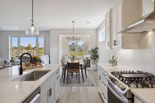 kitchen featuring wall chimney range hood, appliances with stainless steel finishes, light countertops, and a sink