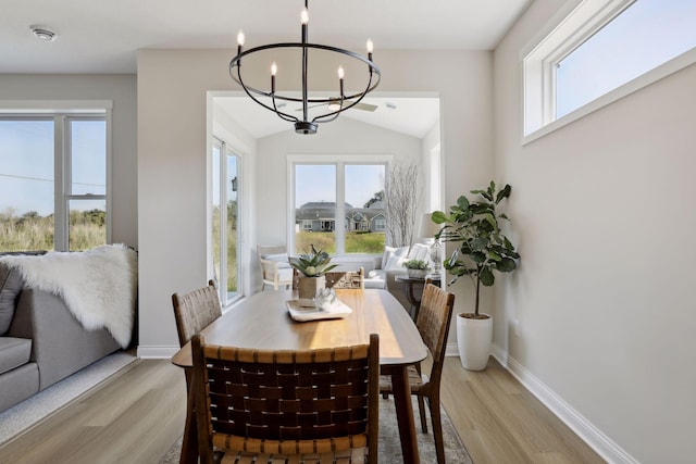 dining area with light wood-type flooring, baseboards, and an inviting chandelier