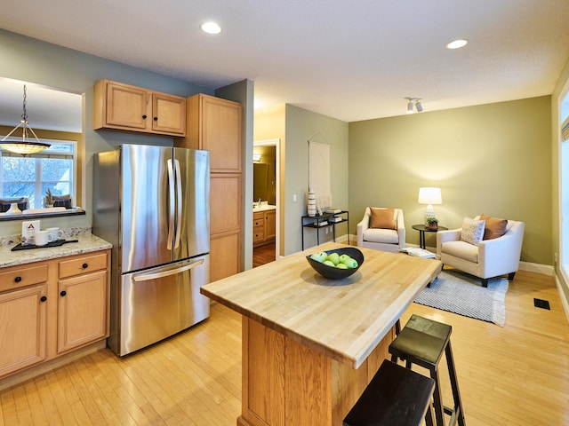 kitchen with stainless steel fridge, a kitchen breakfast bar, a center island, light hardwood / wood-style floors, and decorative light fixtures