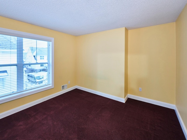 spare room featuring dark carpet and a textured ceiling