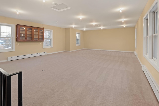 empty room featuring a baseboard heating unit, attic access, light carpet, and baseboards