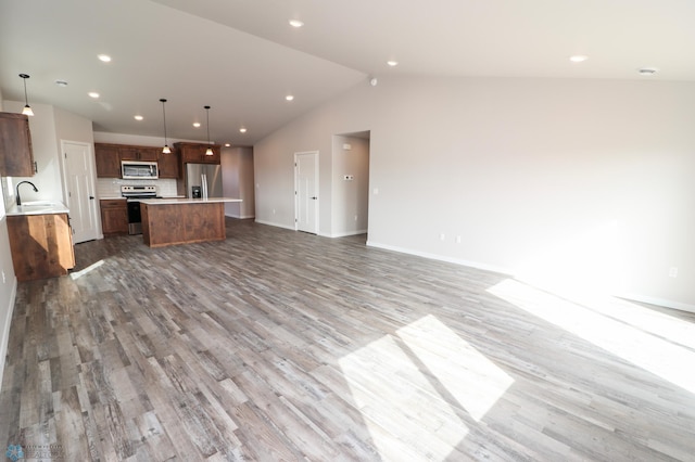 unfurnished living room with hardwood / wood-style flooring, decorative light fixtures, vaulted ceiling, a kitchen island, and sink