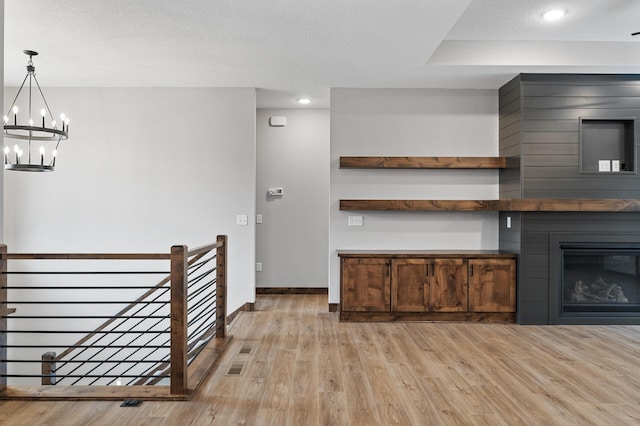 kitchen with pendant lighting, a large fireplace, a chandelier, a textured ceiling, and light hardwood / wood-style flooring