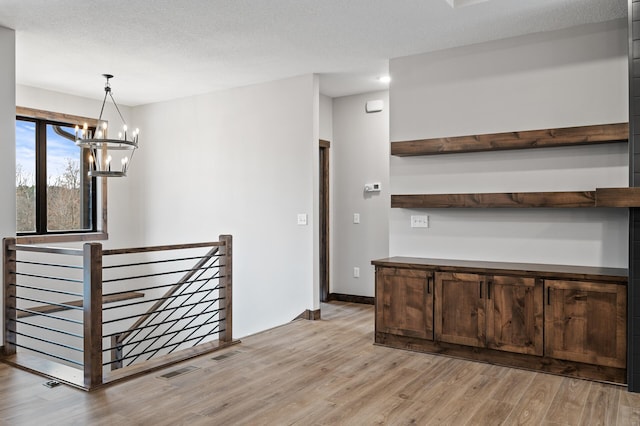 interior space featuring a chandelier, dark brown cabinets, light hardwood / wood-style flooring, a textured ceiling, and pendant lighting