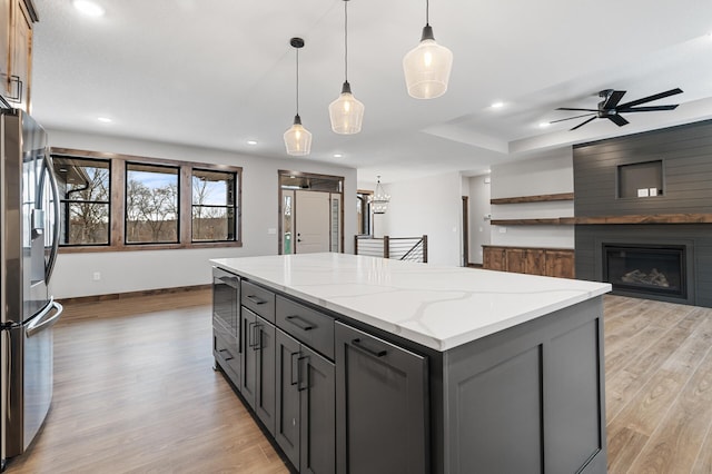 kitchen with stainless steel refrigerator with ice dispenser, a center island, gray cabinets, pendant lighting, and light stone countertops