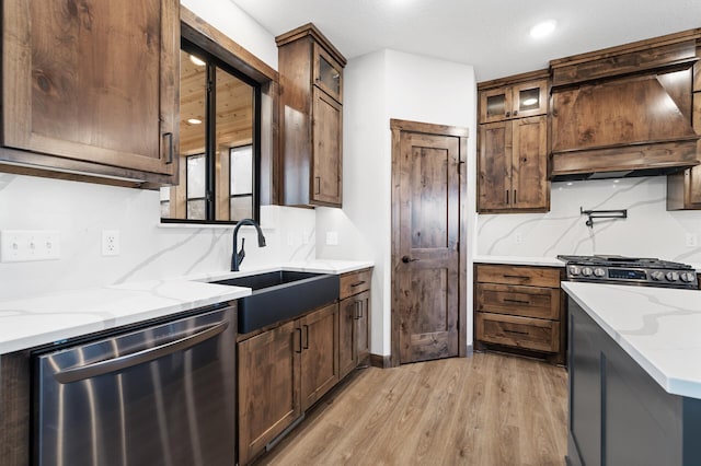 kitchen with premium range hood, stainless steel dishwasher, light stone countertops, and sink