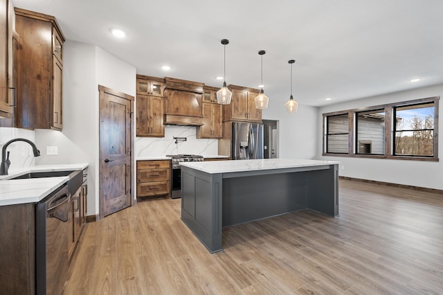 kitchen with a kitchen island, pendant lighting, sink, stainless steel appliances, and custom range hood