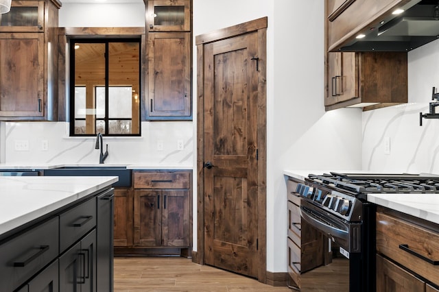 kitchen with light stone counters, black range with gas stovetop, light hardwood / wood-style floors, and extractor fan