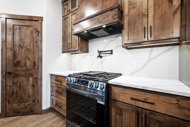 kitchen with gas stove, premium range hood, light stone counters, and light hardwood / wood-style floors