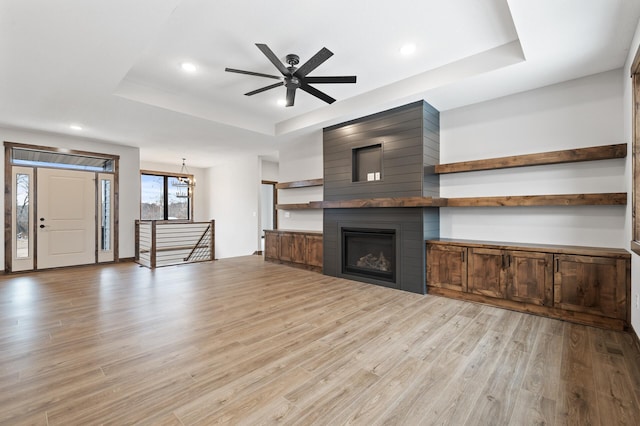 unfurnished living room with a large fireplace, light hardwood / wood-style flooring, ceiling fan, and a tray ceiling