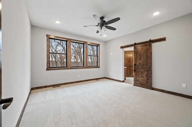 unfurnished bedroom with light carpet, a textured ceiling, a barn door, and ceiling fan