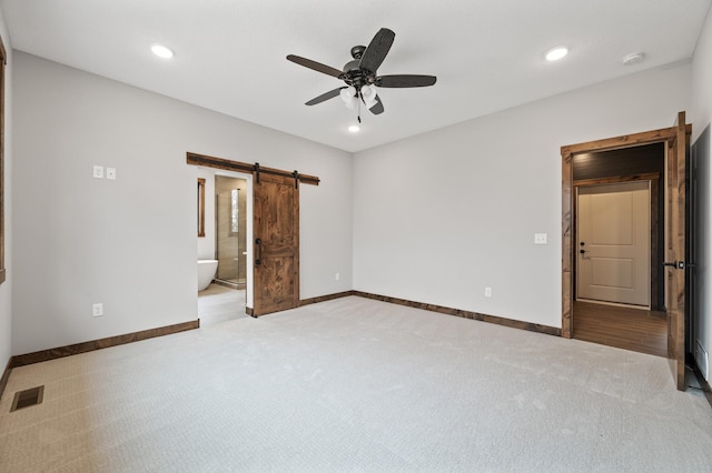 unfurnished bedroom with ceiling fan, a barn door, light colored carpet, and ensuite bath