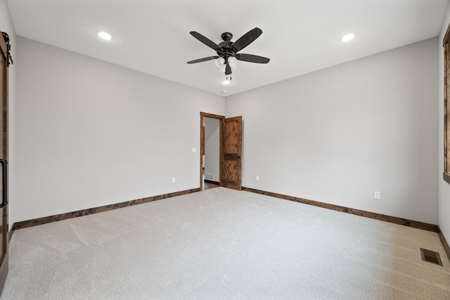 carpeted empty room featuring a barn door and ceiling fan