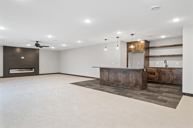 kitchen featuring sink, hanging light fixtures, a large fireplace, dark carpet, and a kitchen island