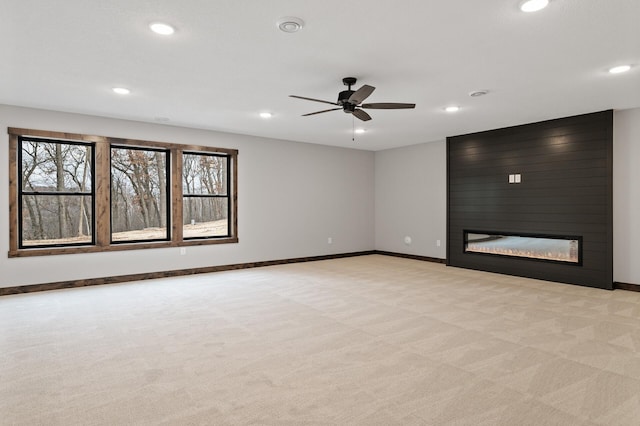 spare room with a large fireplace, light colored carpet, and ceiling fan