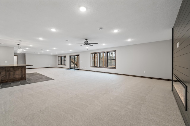 unfurnished living room with light carpet, a textured ceiling, and ceiling fan