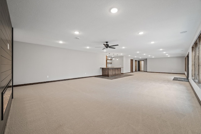 unfurnished living room featuring bar, light colored carpet, a textured ceiling, and ceiling fan