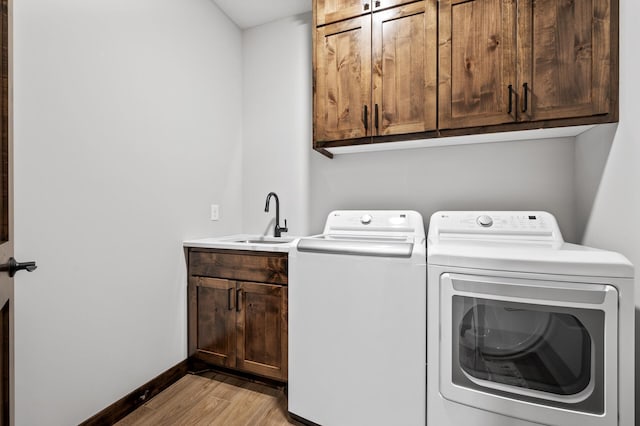 laundry area featuring cabinets, washer and clothes dryer, sink, and light hardwood / wood-style flooring