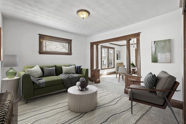 living room with decorative columns, baseboards, a textured ceiling, and light colored carpet