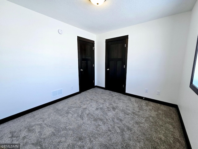 carpeted empty room featuring a textured ceiling, visible vents, and baseboards