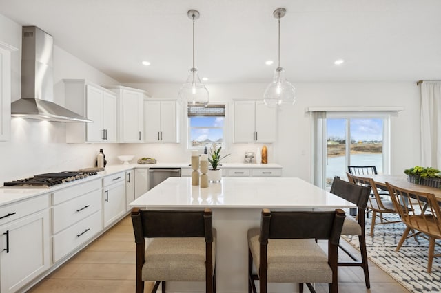 kitchen featuring a water view, white cabinetry, hanging light fixtures, stainless steel appliances, and wall chimney range hood