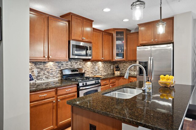 kitchen featuring brown cabinetry, a center island with sink, a sink, decorative backsplash, and stainless steel appliances