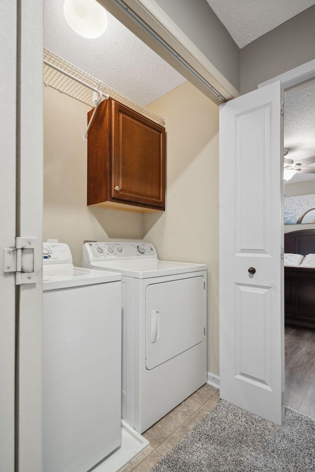 laundry area featuring a textured ceiling, light tile patterned flooring, cabinet space, and washing machine and clothes dryer