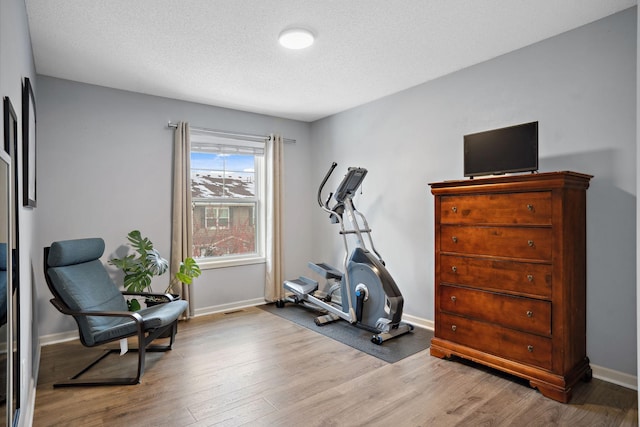 exercise room with baseboards, a textured ceiling, and wood finished floors