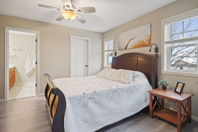 bedroom with connected bathroom, baseboards, light wood-style floors, and ceiling fan