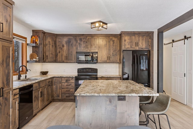 kitchen with black appliances, a sink, open shelves, a center island, and a barn door