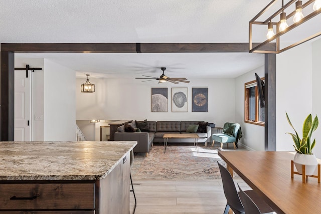 living area featuring light wood-type flooring, beam ceiling, a ceiling fan, a textured ceiling, and a barn door