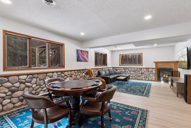 dining area featuring visible vents, a textured ceiling, wood finished floors, a glass covered fireplace, and wainscoting