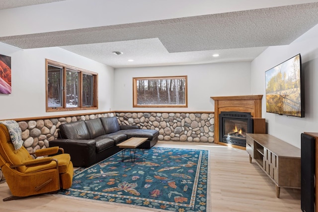 living room with a textured ceiling, recessed lighting, wainscoting, a glass covered fireplace, and light wood-type flooring