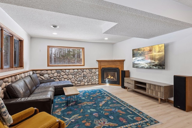 living room featuring wood finished floors, visible vents, recessed lighting, a textured ceiling, and a glass covered fireplace