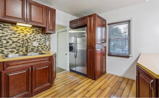 kitchen featuring stainless steel fridge, sink, decorative backsplash, and light wood-type flooring