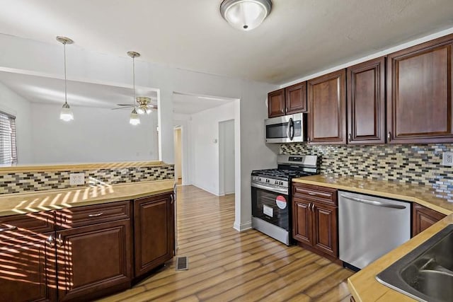 kitchen with hanging light fixtures, decorative backsplash, light hardwood / wood-style floors, and appliances with stainless steel finishes