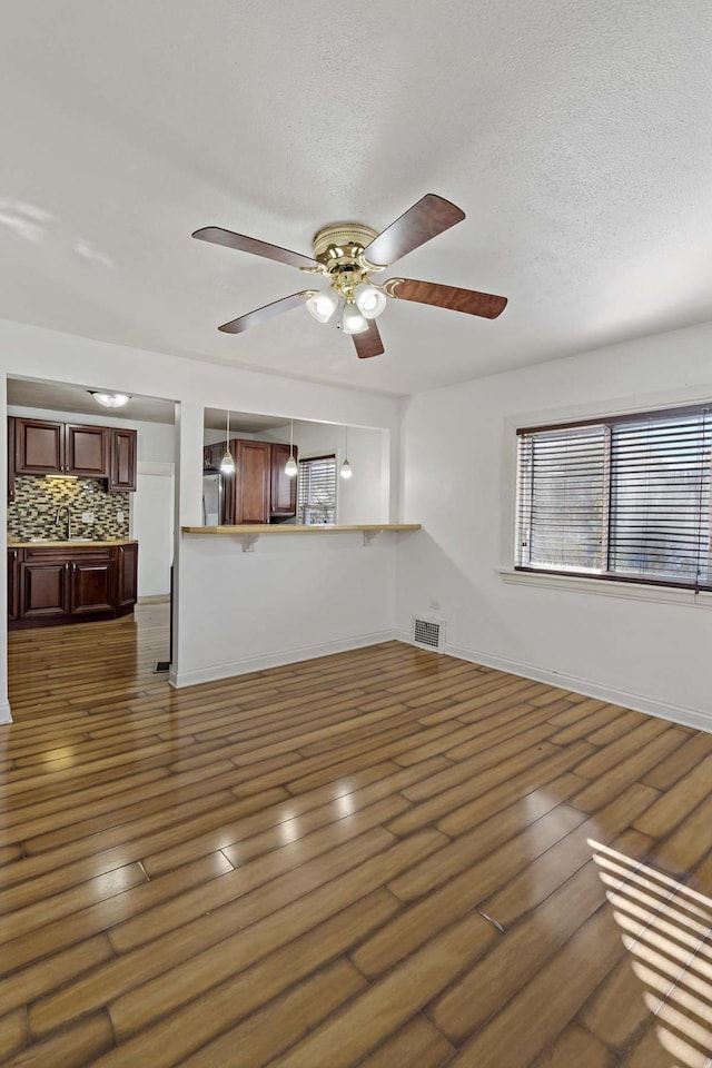 unfurnished living room featuring ceiling fan, dark wood-type flooring, sink, and a textured ceiling