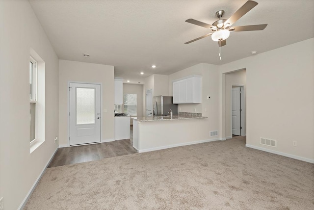 kitchen with white cabinetry, light stone counters, stainless steel refrigerator, kitchen peninsula, and light colored carpet